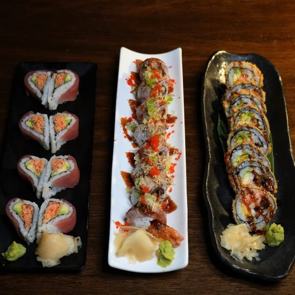Three platters of sushi rolls, including heart-shaped, topped, and fried varieties, with ginger and wasabi.
