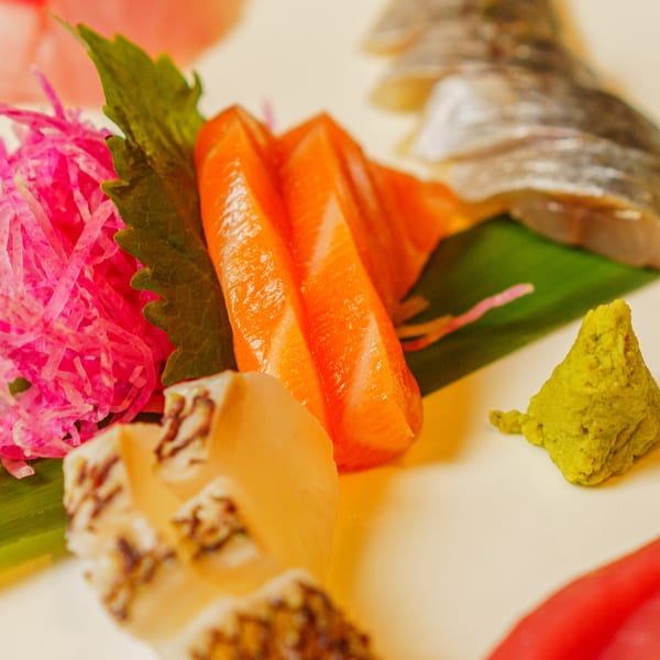Kanpai sushi platter with salmon sashimi, white fish, pink radish, and wasabi.