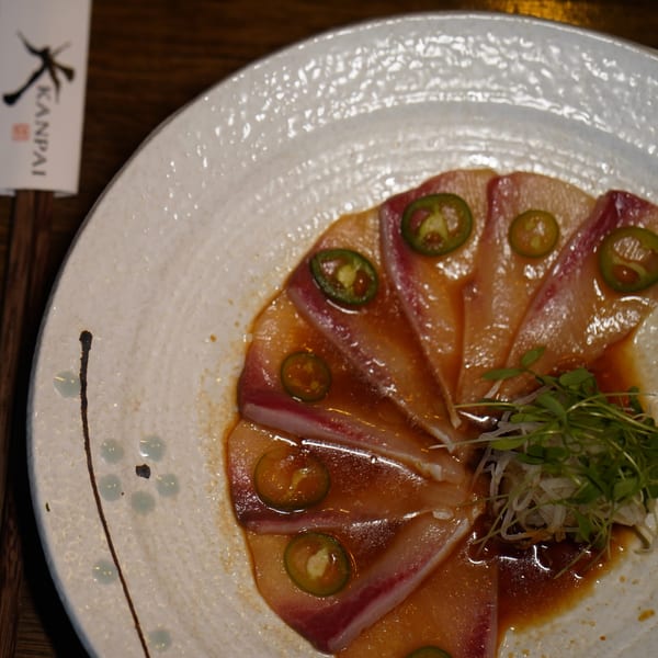 Kanpai's yellowtail sashimi with jalapeño slices, microgreens, and ponzu sauce on a white plate.