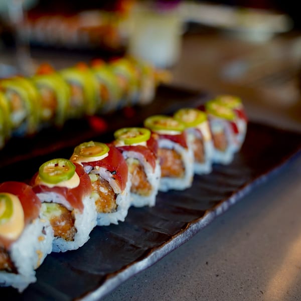 Two plates of Kanpai sushi rolls, one topped with tuna and jalapeños, the other with avocado.