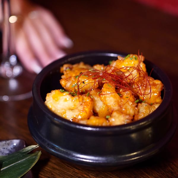 Kanpai's crispy shrimp in a black bowl, garnished with chili threads and chives.
