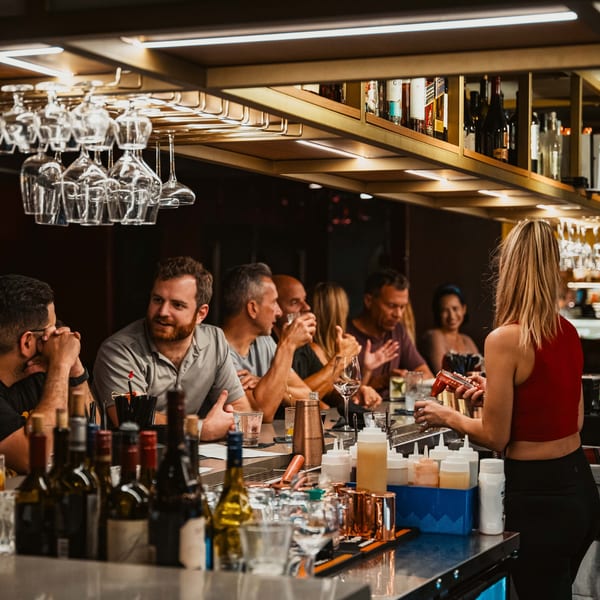 Customers seated at Kanpai's bar, with a bartender preparing drinks and bottles on shelves.