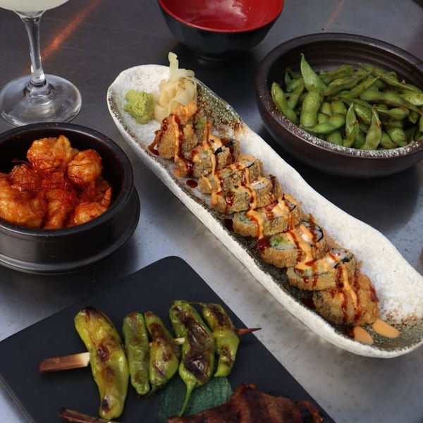 Kanpai's fried sushi rolls, edamame, spicy shrimp, and grilled peppers on a dark table.